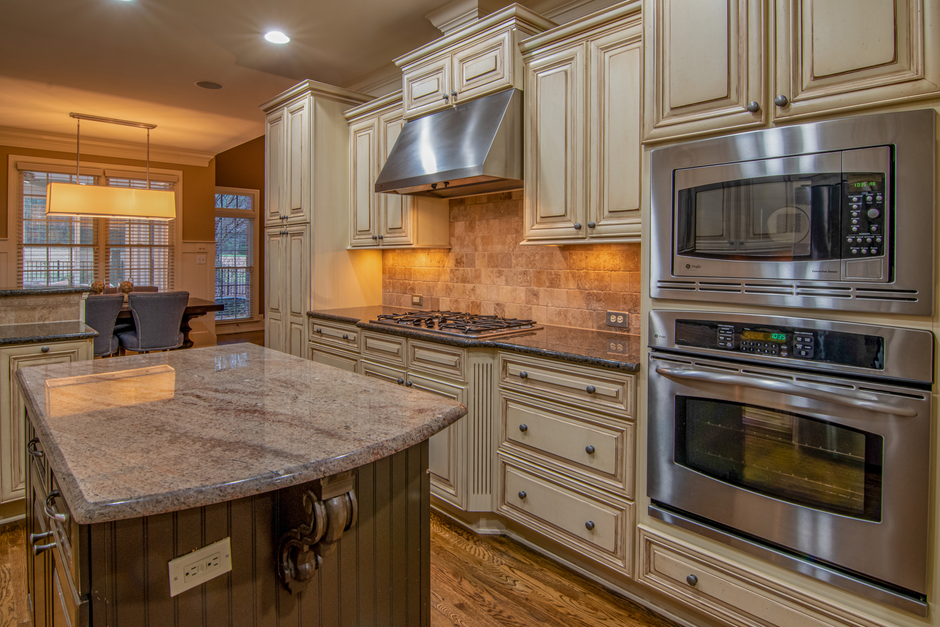 A modern kitchen featuring a beige wooden cabinetry with detailed molding, a granite countertop island, and built-in stainless steel appliances including a microwave and oven. The countertop appears c